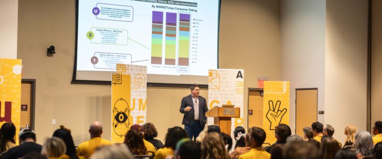 A presenter at Arizona State University standing at a podium in front of an audience, pointing to a slide displaying three stacked bar charts.